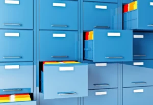 A wall of blue filing cabinets with four pulled out diagonally and multicolored file folders